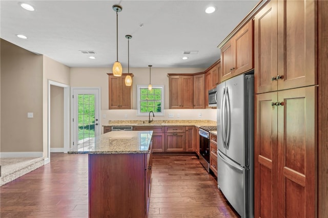 kitchen featuring sink, stainless steel appliances, a center island, light stone counters, and decorative light fixtures