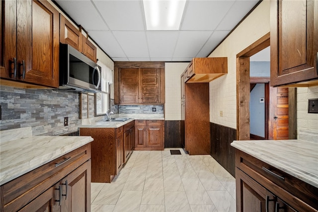 kitchen featuring sink, a drop ceiling, light stone counters, and decorative backsplash