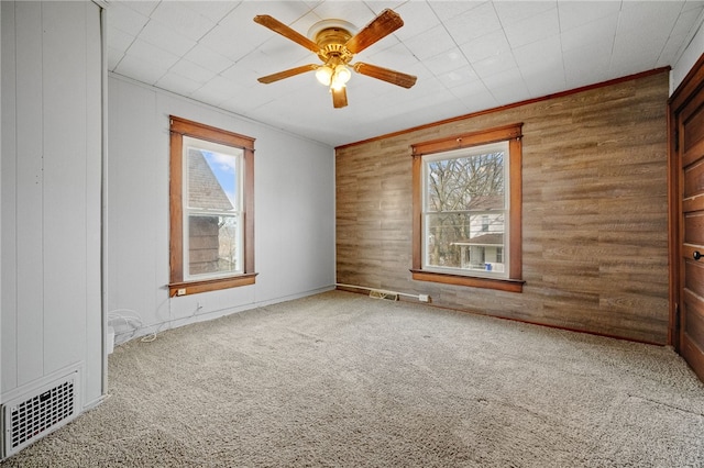 carpeted spare room with crown molding, ceiling fan, and wood walls