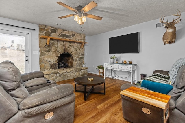 living room with ceiling fan, a fireplace, a textured ceiling, and light wood-type flooring