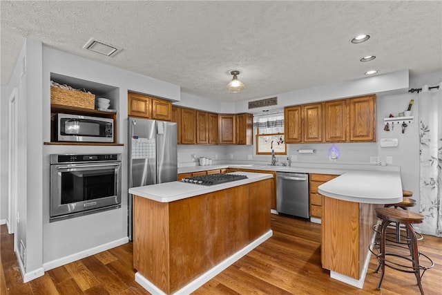 kitchen with a kitchen bar, a textured ceiling, appliances with stainless steel finishes, dark hardwood / wood-style floors, and a kitchen island