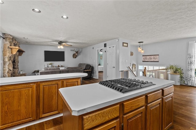 kitchen featuring pendant lighting, dark wood-type flooring, a textured ceiling, a kitchen island, and stainless steel gas stovetop