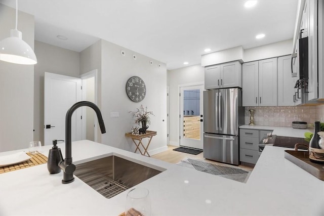 kitchen with gray cabinets, stainless steel refrigerator, decorative light fixtures, sink, and backsplash