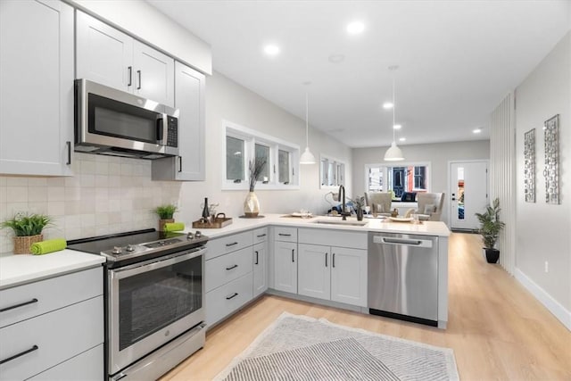 kitchen with appliances with stainless steel finishes, pendant lighting, sink, kitchen peninsula, and light hardwood / wood-style flooring