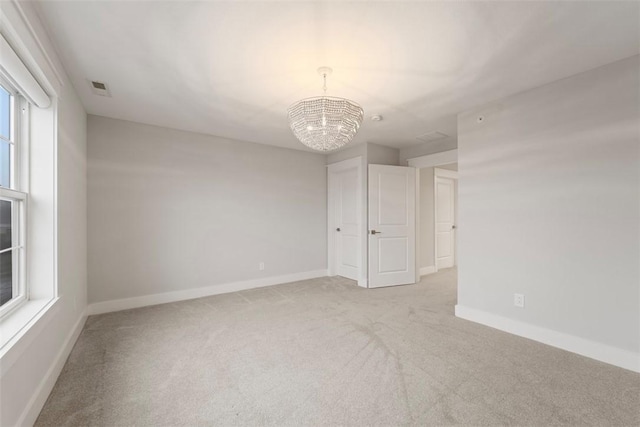 unfurnished room featuring an inviting chandelier and light colored carpet