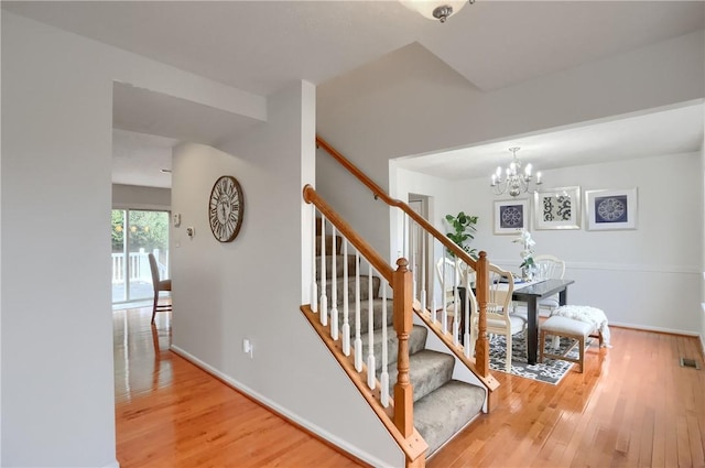 stairs with hardwood / wood-style flooring and an inviting chandelier