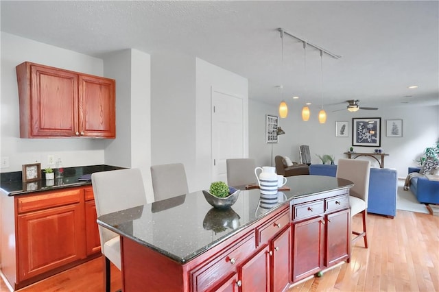 kitchen with dark stone countertops, a breakfast bar area, a center island, ceiling fan, and light wood-type flooring