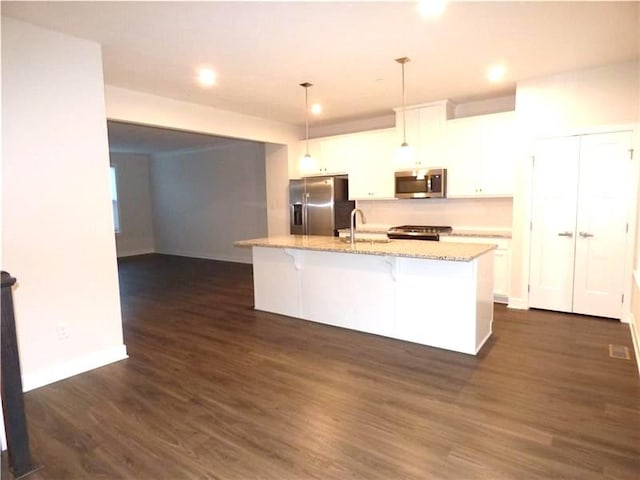 kitchen featuring a breakfast bar, white cabinetry, decorative light fixtures, stainless steel appliances, and a kitchen island with sink