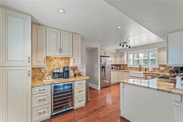 kitchen with appliances with stainless steel finishes, beverage cooler, decorative backsplash, hardwood / wood-style flooring, and light stone counters