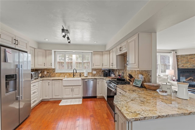 kitchen with white cabinetry, backsplash, stainless steel appliances, light stone countertops, and light hardwood / wood-style floors