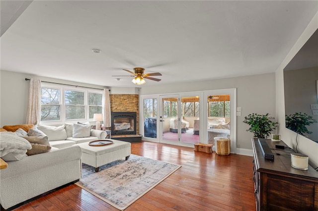 living room featuring hardwood / wood-style flooring, ceiling fan, and a stone fireplace