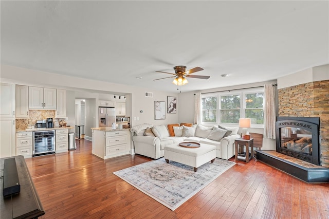 living room featuring wine cooler, a stone fireplace, light hardwood / wood-style flooring, and ceiling fan