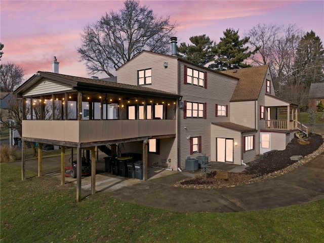 back house at dusk featuring a carport, a sunroom, and central air condition unit