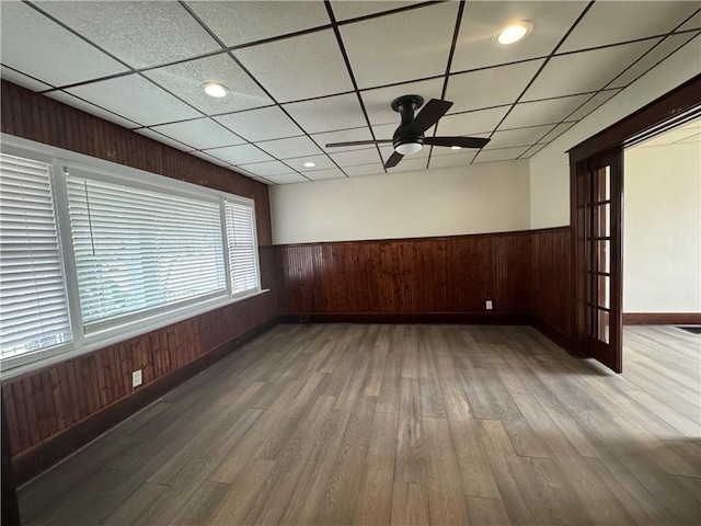 empty room with wood-type flooring, a paneled ceiling, ceiling fan, and wooden walls