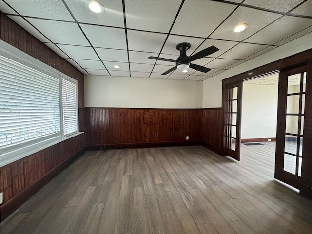 empty room featuring wood-type flooring, a paneled ceiling, wooden walls, and french doors