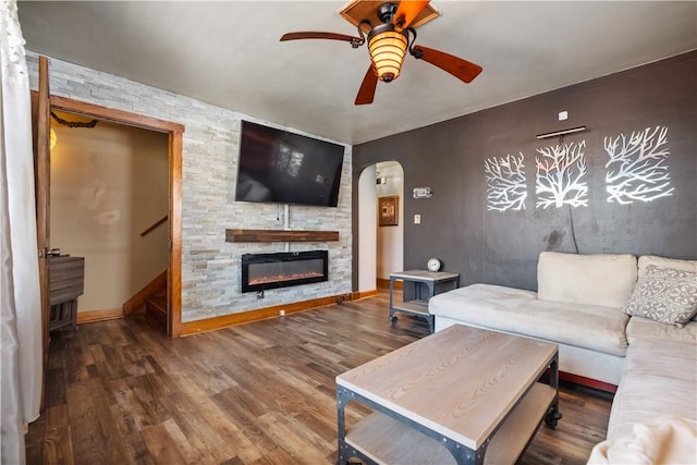 living room featuring a stone fireplace, dark wood-type flooring, and ceiling fan