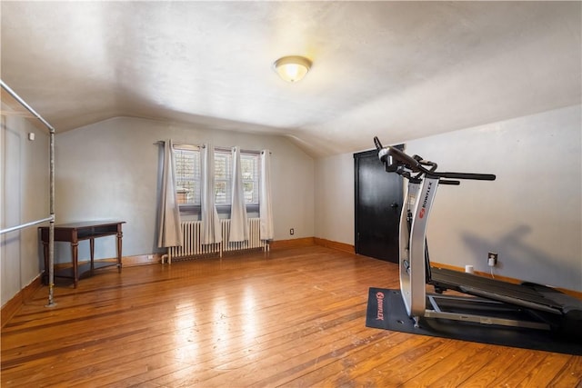 exercise room featuring vaulted ceiling, radiator, and hardwood / wood-style floors