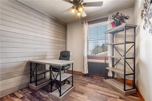 home office with hardwood / wood-style flooring, radiator heating unit, ceiling fan, and wood walls