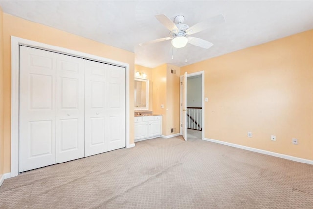 unfurnished bedroom featuring ensuite bath, light colored carpet, ceiling fan, and a closet