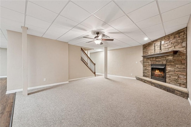 basement featuring a stone fireplace, carpet floors, a paneled ceiling, and ceiling fan