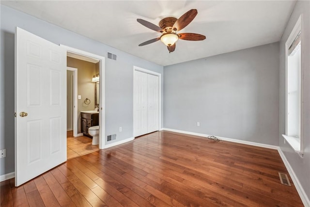 unfurnished bedroom with hardwood / wood-style flooring, ensuite bath, ceiling fan, and a closet