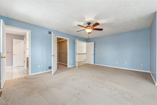 unfurnished bedroom featuring light carpet, a walk in closet, a closet, and ceiling fan