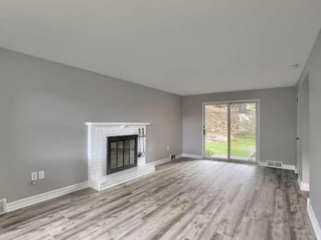 unfurnished living room featuring a brick fireplace and light wood-type flooring