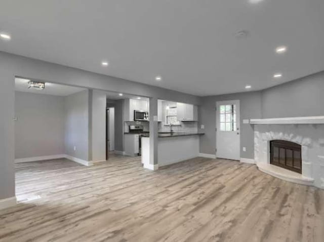 unfurnished living room featuring a stone fireplace and light wood-type flooring