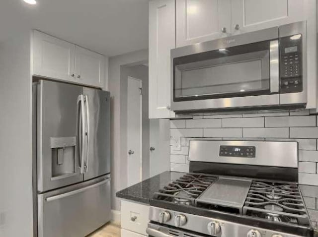 kitchen featuring dark stone countertops, appliances with stainless steel finishes, backsplash, and white cabinets