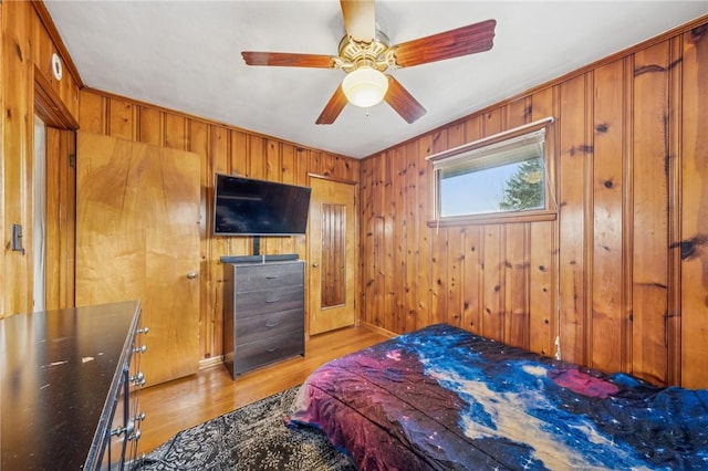 bedroom featuring ceiling fan, light hardwood / wood-style floors, and wood walls