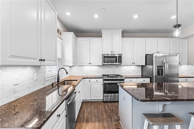 kitchen with appliances with stainless steel finishes, sink, white cabinets, dark stone counters, and hanging light fixtures