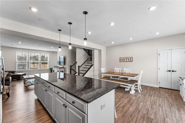 kitchen featuring gray cabinets, dark hardwood / wood-style floors, pendant lighting, dark stone counters, and a center island