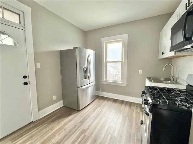 kitchen with sink, light hardwood / wood-style flooring, appliances with stainless steel finishes, backsplash, and white cabinets