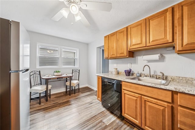 kitchen featuring sink, light wood-type flooring, stainless steel refrigerator, dishwasher, and light stone countertops