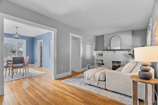 living room with an inviting chandelier, a brick fireplace, and light hardwood / wood-style floors