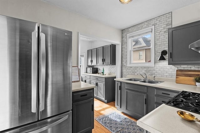 kitchen with sink, gray cabinetry, light wood-type flooring, stainless steel refrigerator, and decorative backsplash