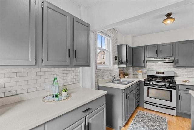 kitchen with tasteful backsplash, sink, gray cabinetry, light hardwood / wood-style floors, and stainless steel gas range