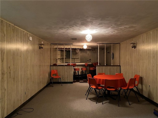 dining space featuring light carpet, wood walls, and indoor bar