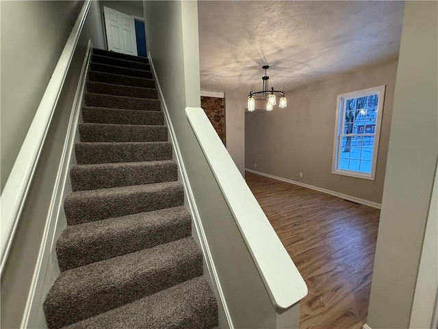 stairs with wood-type flooring and an inviting chandelier