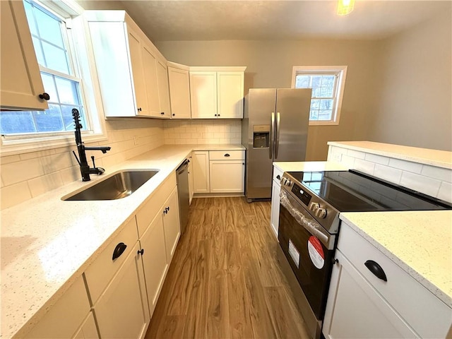 kitchen featuring white cabinetry, appliances with stainless steel finishes, sink, and light stone counters