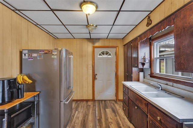 kitchen with hardwood / wood-style floors, wooden walls, stainless steel refrigerator, sink, and a drop ceiling