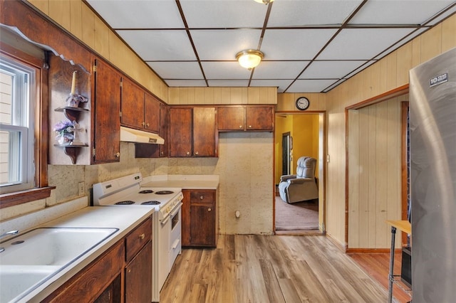 kitchen with electric stove, sink, stainless steel refrigerator, a drop ceiling, and light wood-type flooring