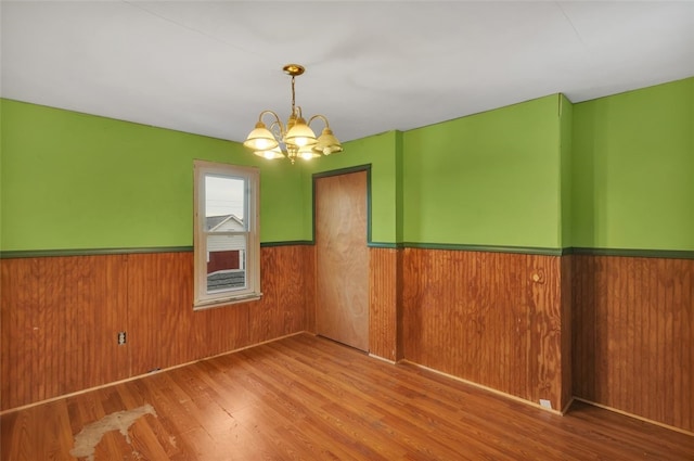 spare room with wood-type flooring, a chandelier, and wood walls