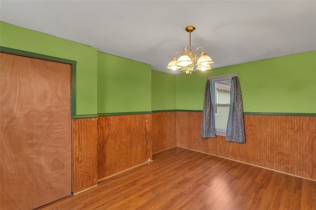 unfurnished room with a chandelier, hardwood / wood-style floors, and wood walls