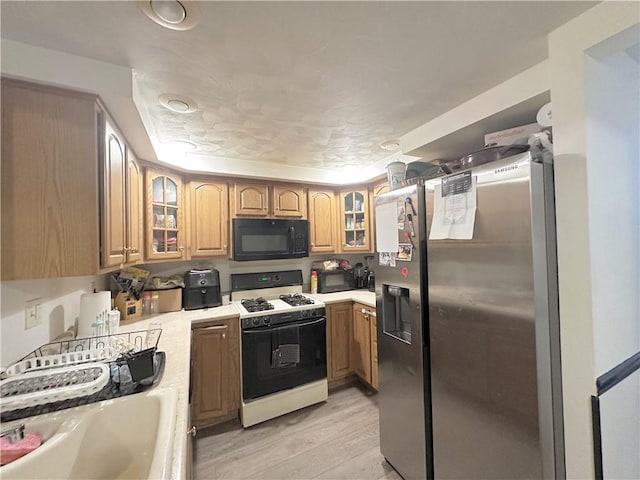 kitchen with stainless steel fridge with ice dispenser, gas range, sink, and light wood-type flooring