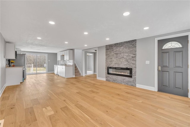 unfurnished living room with a stone fireplace and light wood-type flooring