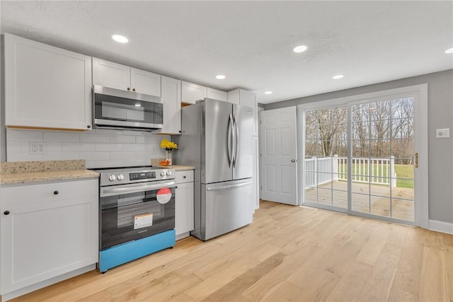 kitchen with backsplash, stainless steel appliances, light stone counters, white cabinets, and light wood-type flooring