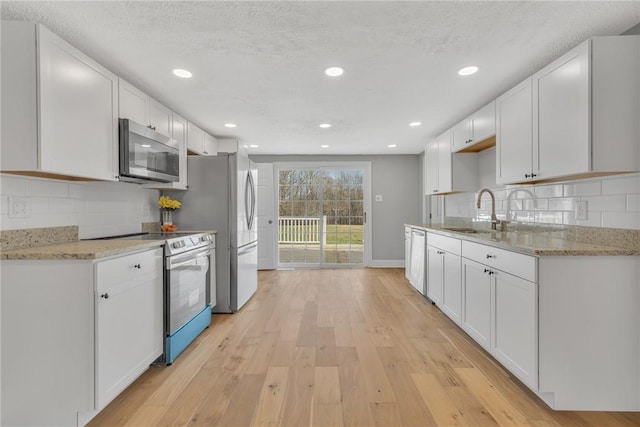 kitchen with sink, white cabinets, decorative backsplash, light hardwood / wood-style floors, and stainless steel appliances