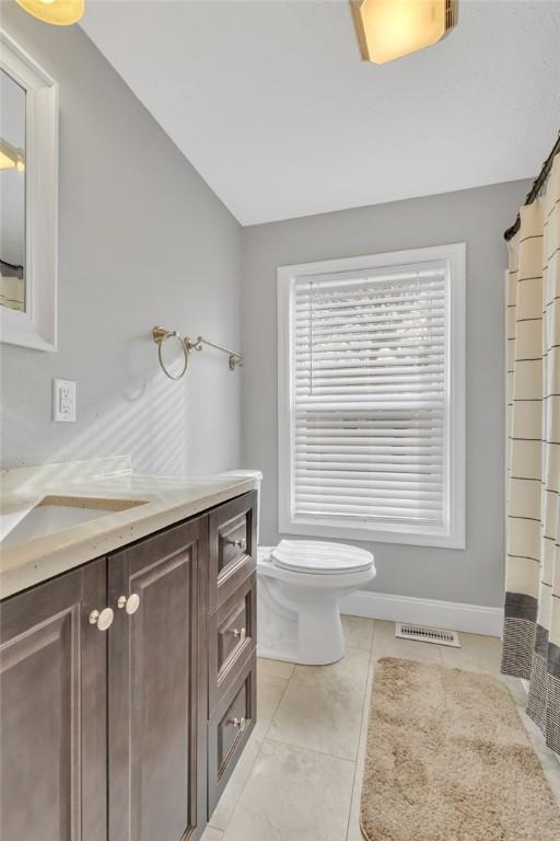 bathroom with vanity, tile patterned flooring, lofted ceiling, and toilet