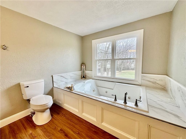 bathroom featuring toilet, wood-type flooring, a bath, and a textured ceiling